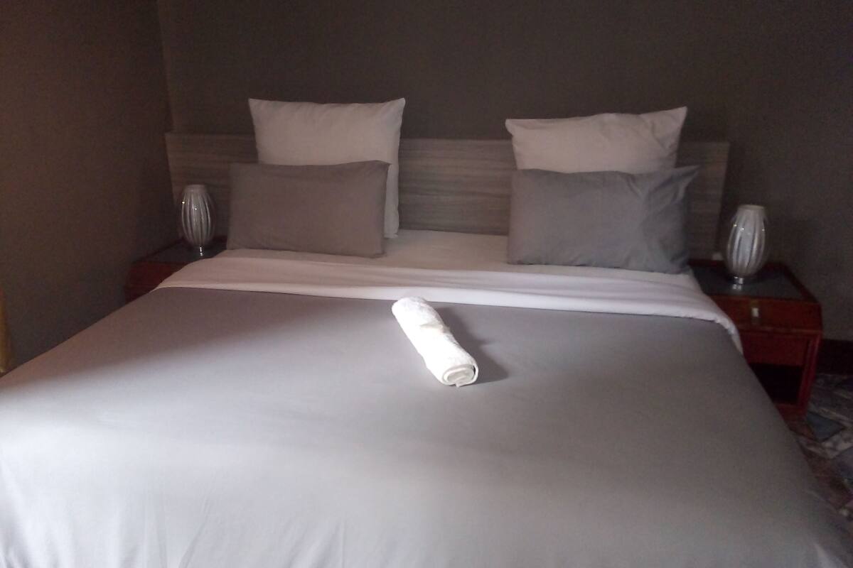 A neatly made bed with a rolled white towel, two bedside tables with lamps, and a headboard with two pillows.