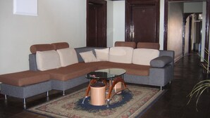 A living room with a sectional sofa, a glass coffee table, and a patterned rug.