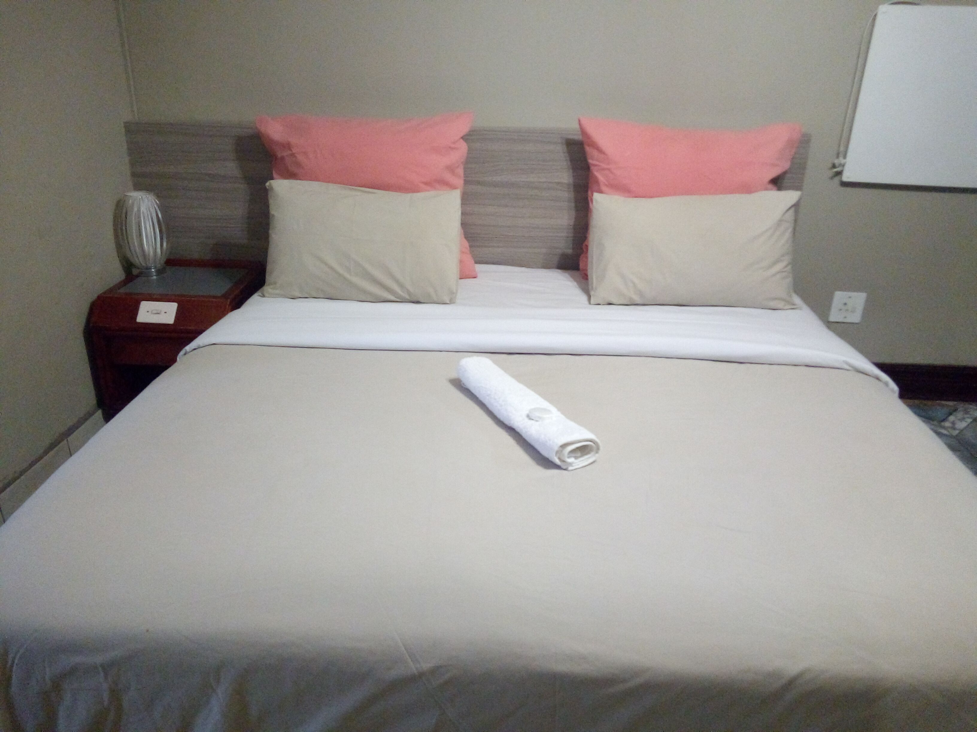 A neatly made bed with a white and beige duvet, two pink pillows, and a rolled white towel on the bed.