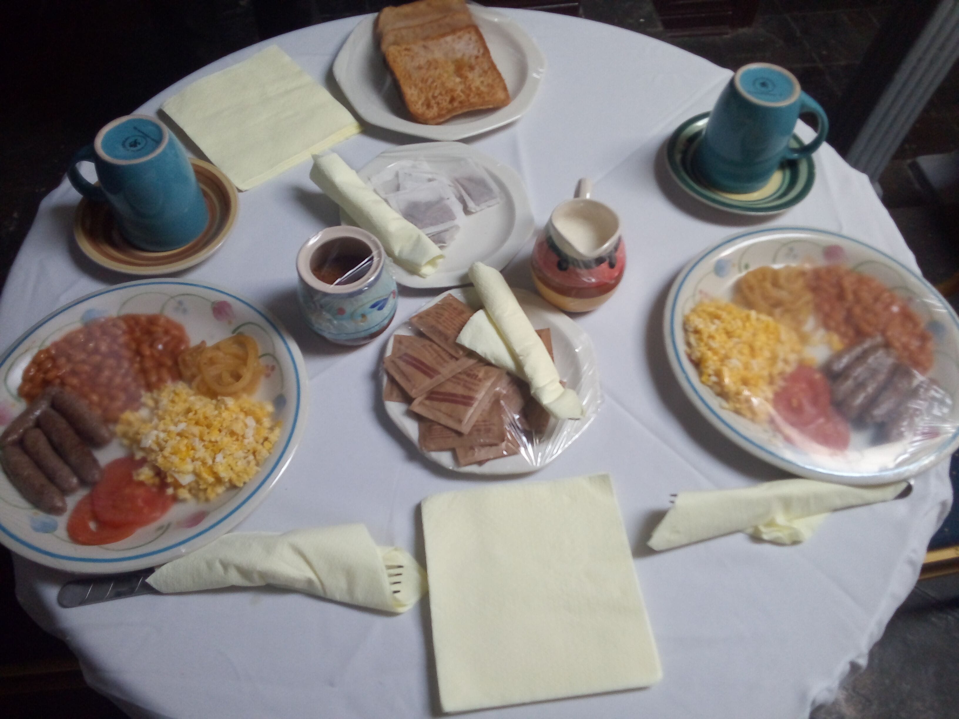 A round table with various breakfast items including eggs, sausages, and bread.