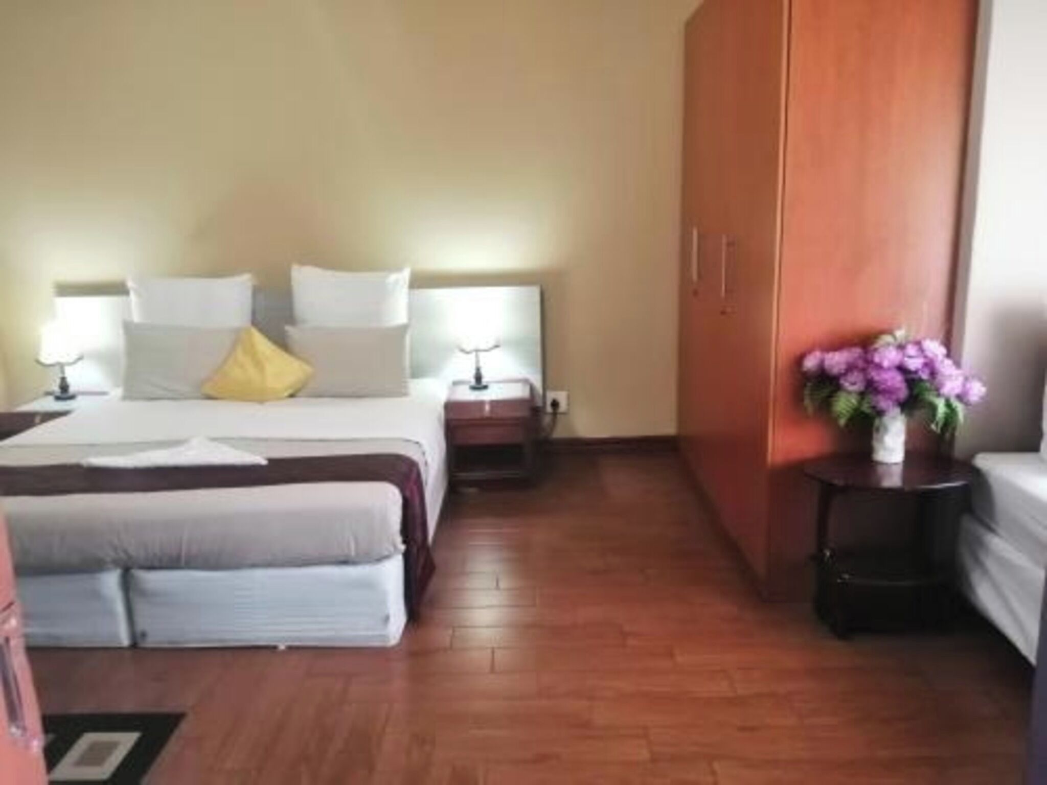 Habitación de hotel con cama, mesitas de noche, armario y una pequeña mesa con un florero.