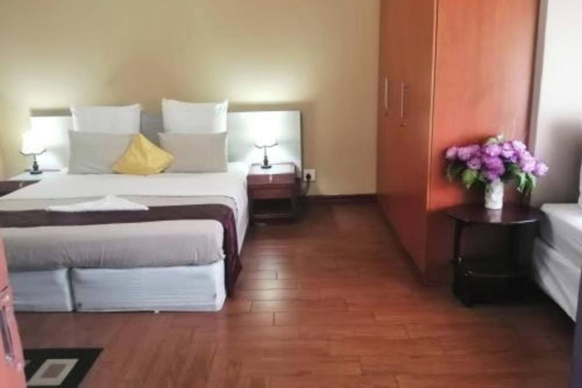 A hotel room with a bed, bedside tables, a wardrobe, and a small table with a vase of flowers.