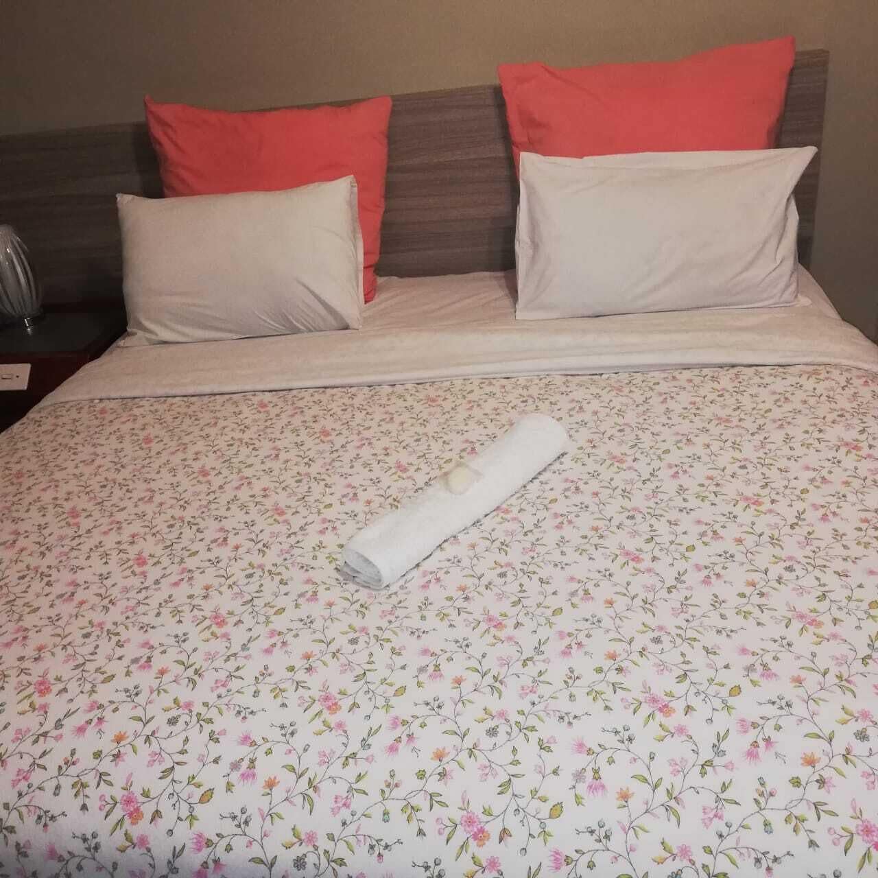 Un lit bien fait, avec une couvre-lit à motifs floraux, deux oreillers et une serviette enroulée.