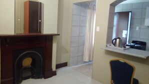 A hotel room with a fireplace, a shower, a sink with a kettle, and a chair.