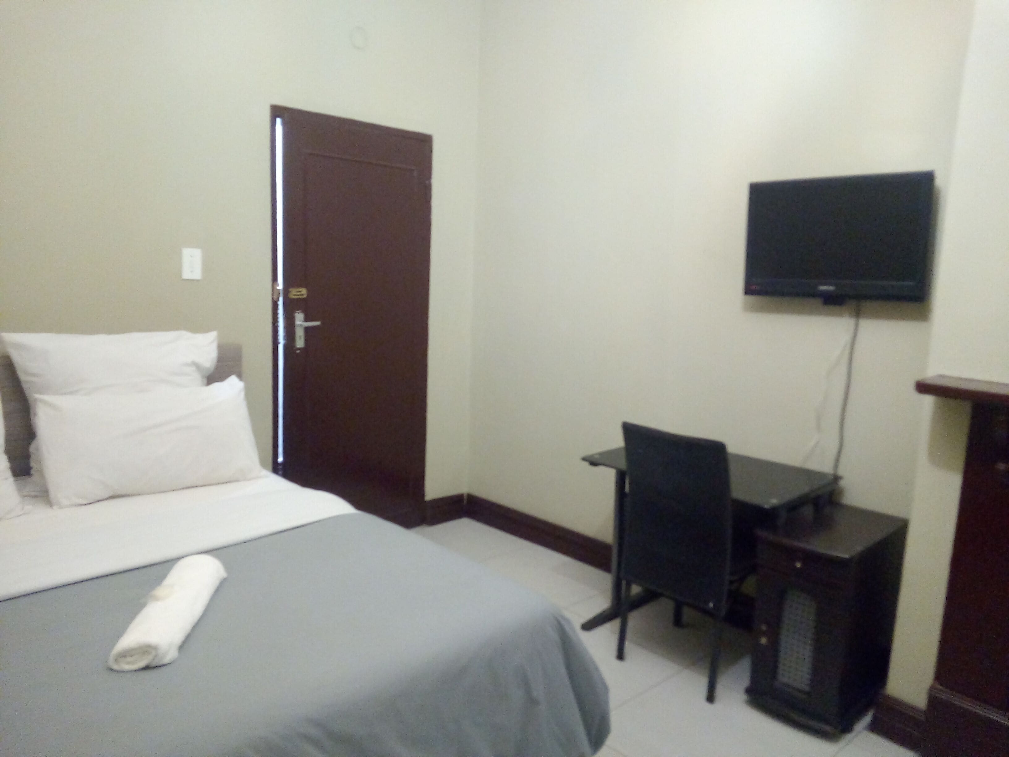 A hotel room with a bed, a desk, a chair, and a television on the wall.