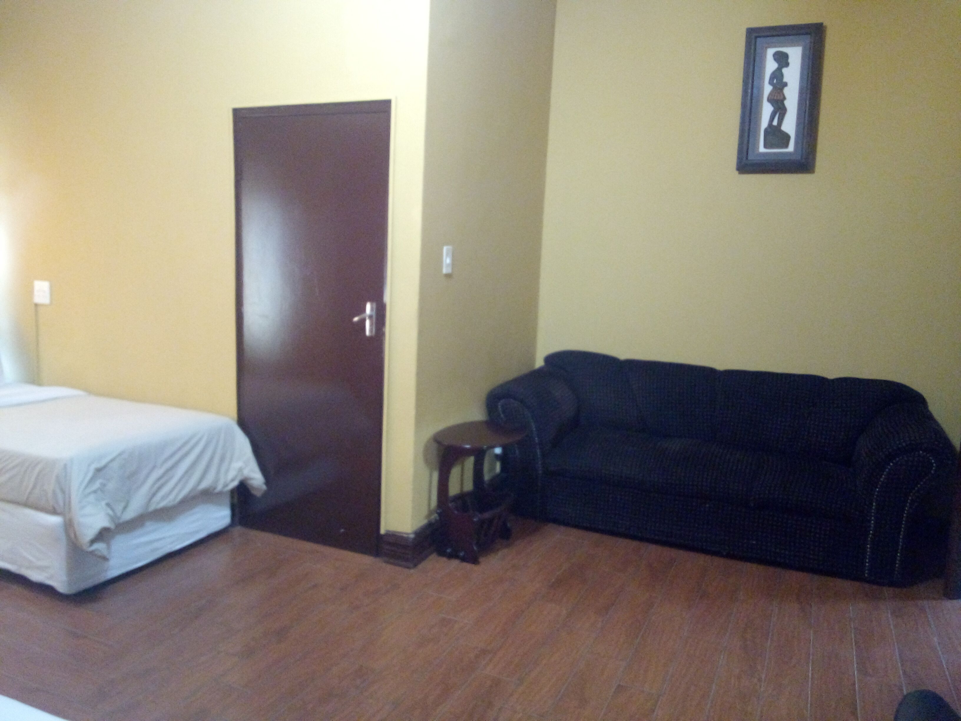 A room with a bed, a dark-colored sofa, a small table, and a door.