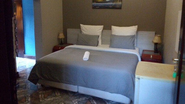 A hotel room with a bed, two bedside tables, a painting on the wall, and a view of the outside.