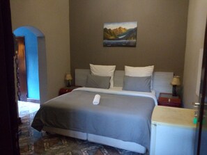 Habitación de hotel con cama, dos mesitas de noche, un cuadro en la pared y vistas al exterior.