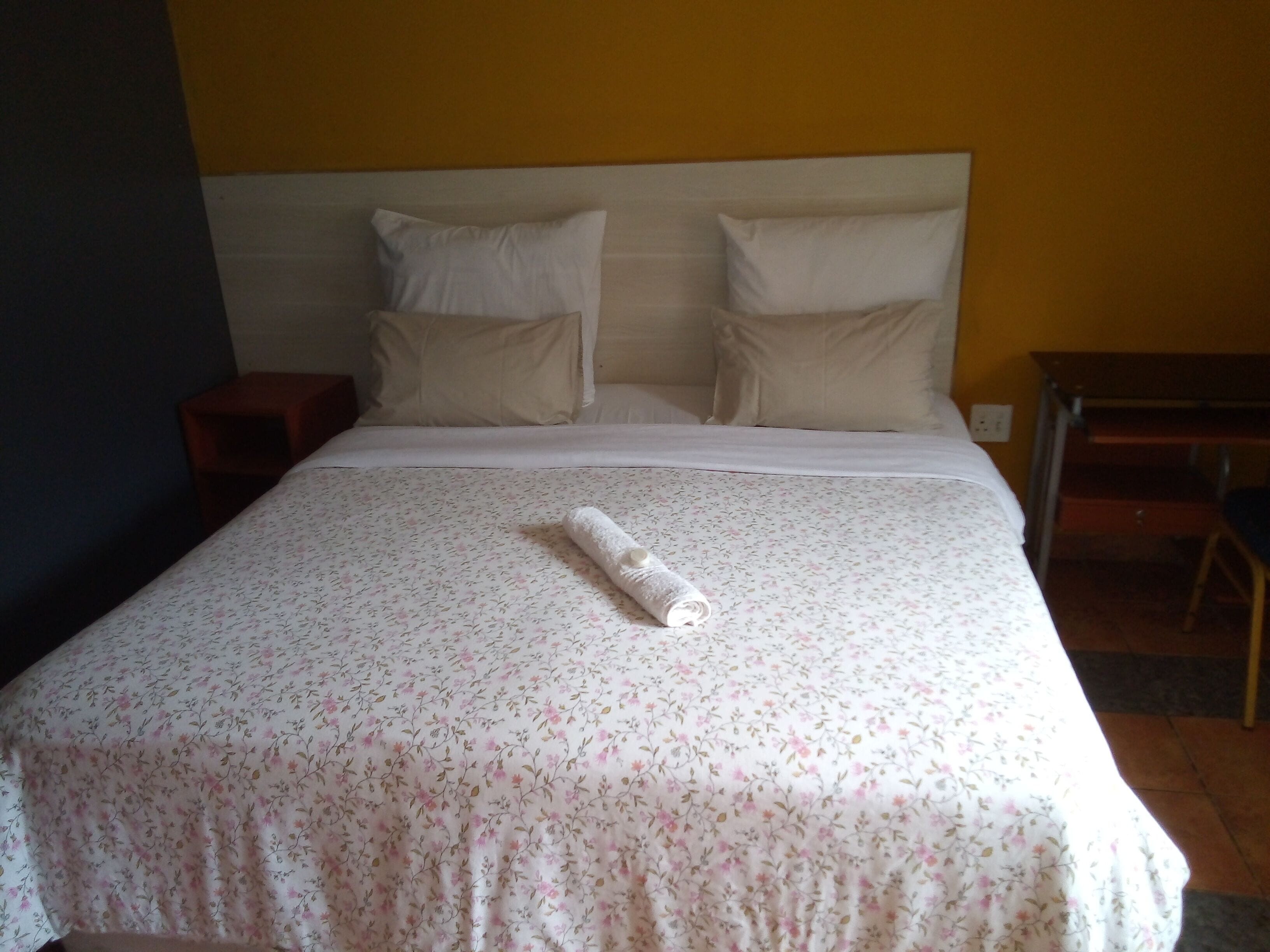 A neatly made bed with a floral bedspread, two pillows, and a rolled towel on the bed.