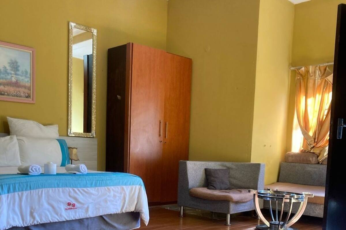 A hotel room with a bed, a wardrobe, a chair, a small table, and a mirror.