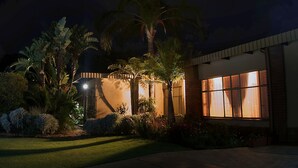 Un edificio residencial bien iluminado con amplios ventanales, rodeado de abundante vegetación y palmeras.