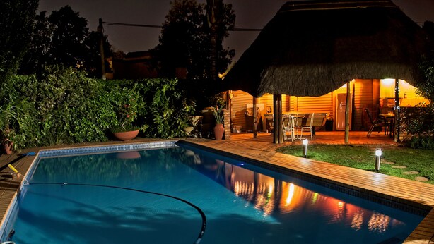 Una piscina con muelle de madera, rodeada de follaje y una estructura con techo de paja.
