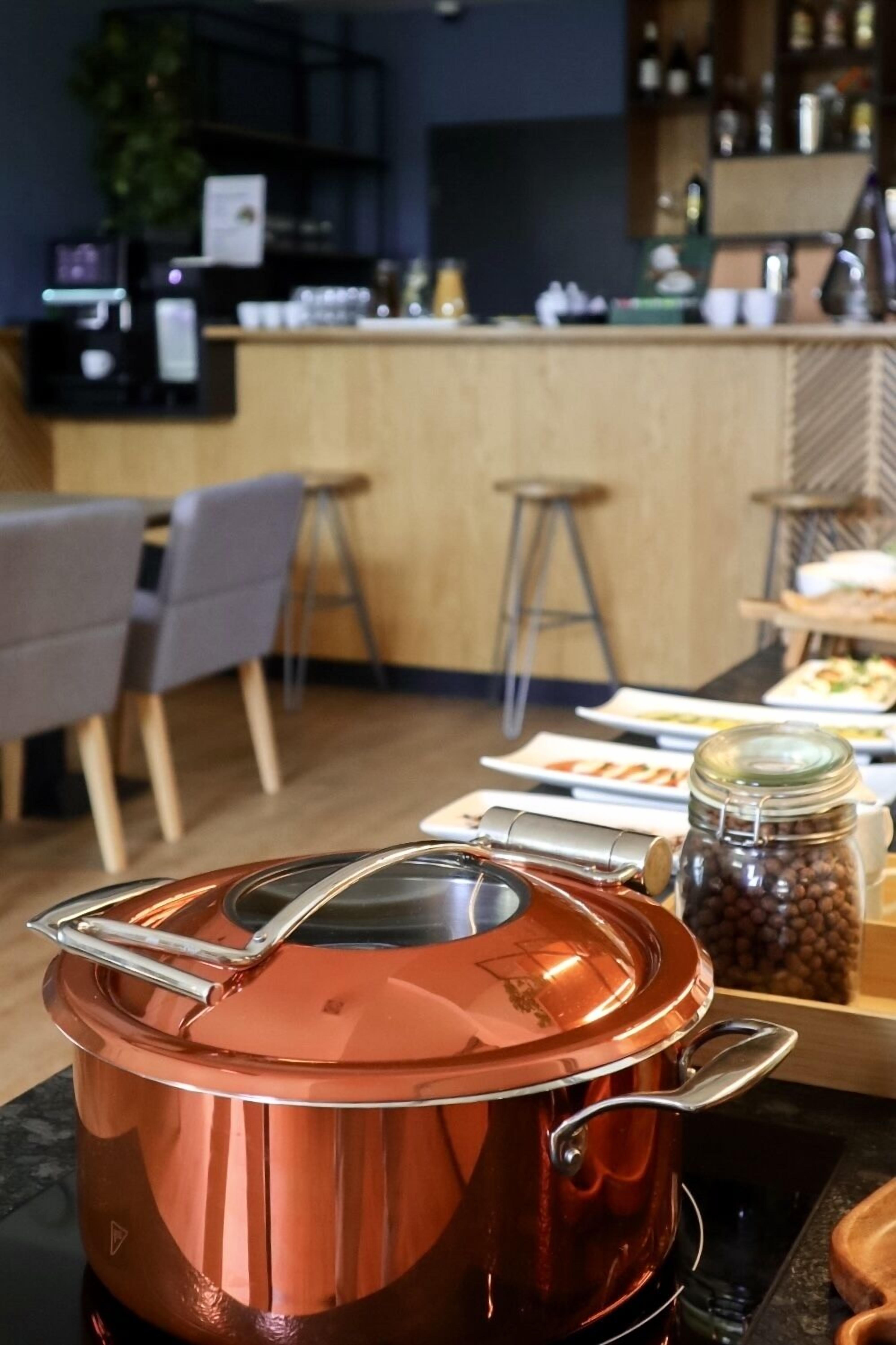 Una cocina con una olla de cobre sobre la hornilla, taburetes de bar de madera y una zona de bar al fondo.