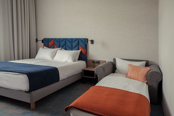 Una habitación de hotel con dos camas, una mesita de noche y un sofá.