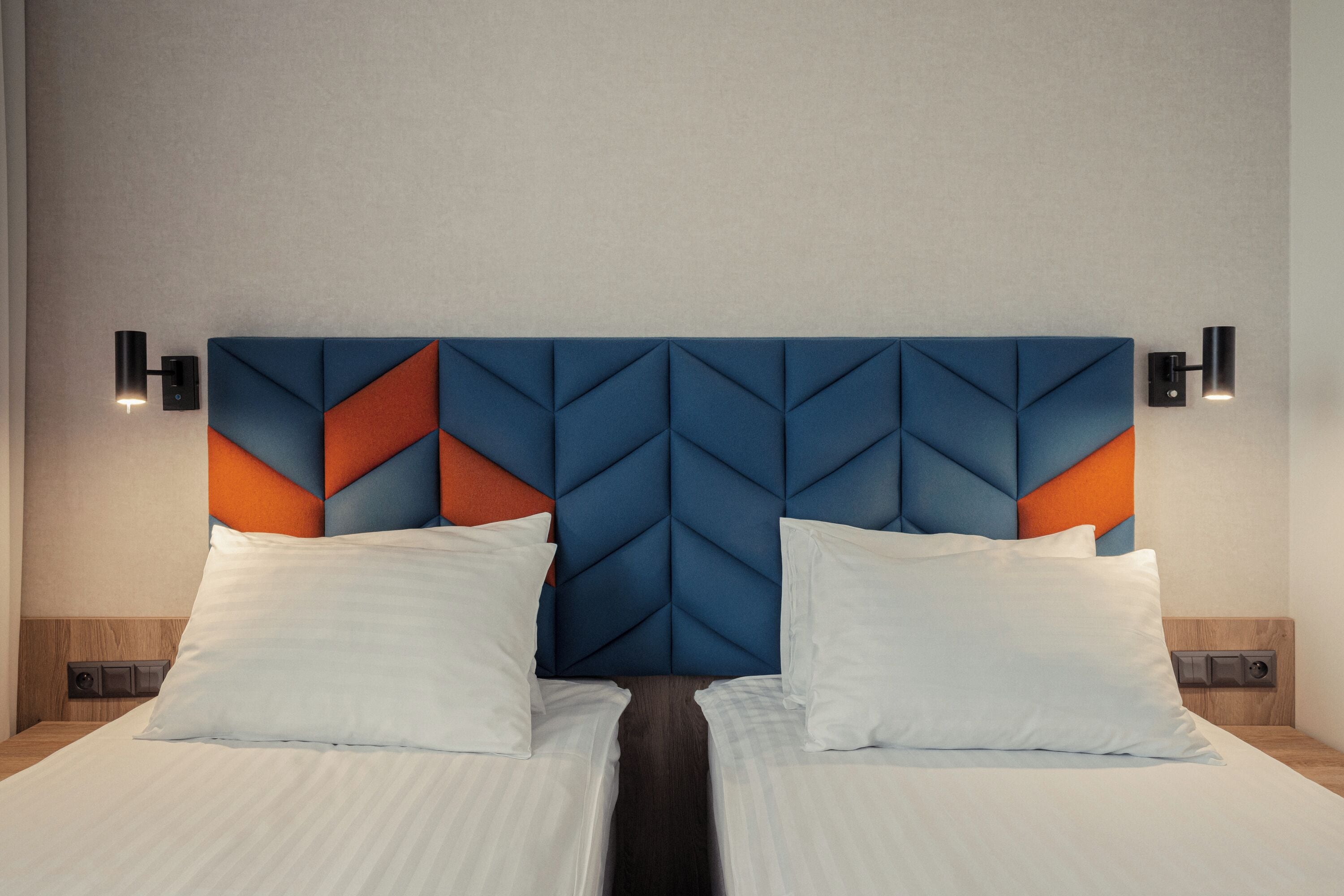 A hotel room with a modern headboard featuring geometric patterns, two white pillows, and bedside lamps.
