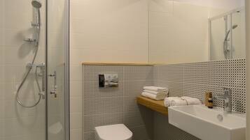 A modern bathroom with a glass shower enclosure, a white toilet, a sink with a mirror, and a wooden shelf with towels.