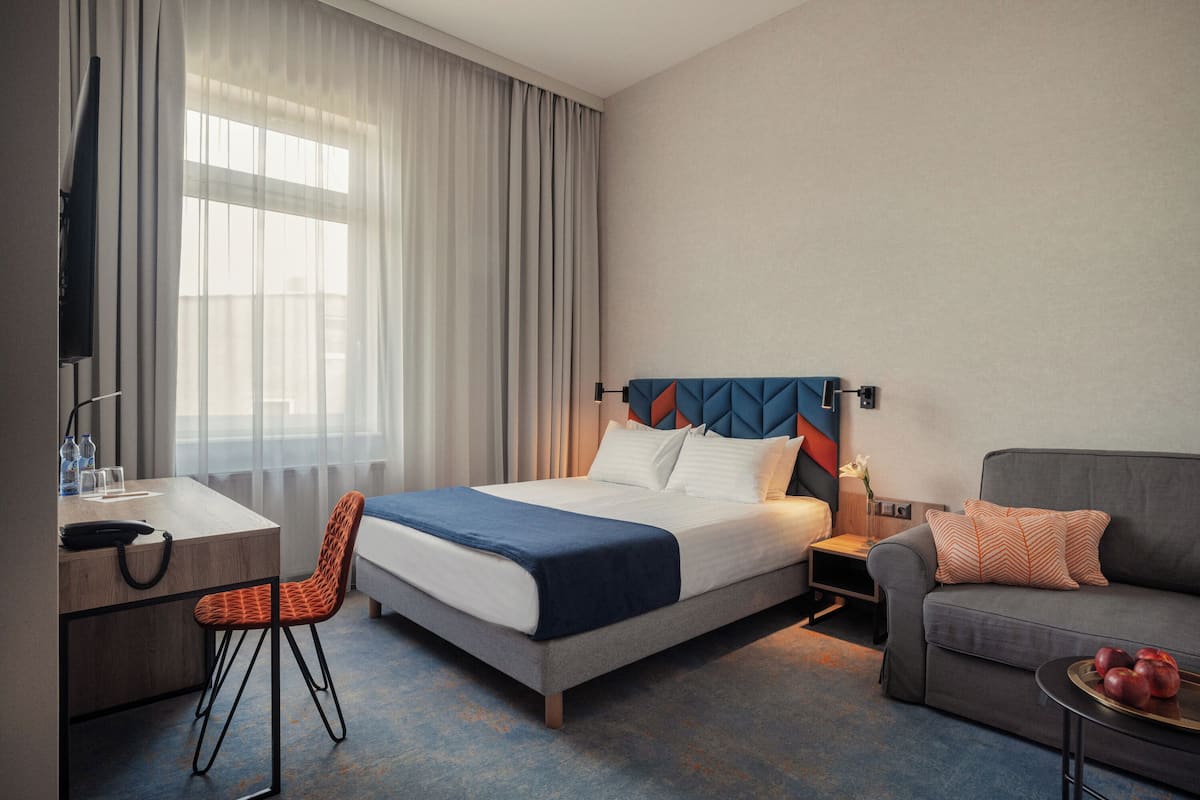 Una habitación de hotel con cama, escritorio, silla, sofá y una mesita con fruta.