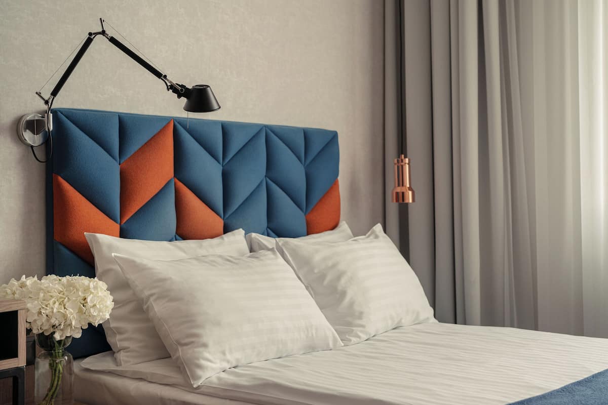 Una cama bien hecha con ropa de cama blanca, un cabecero de estampado geométrico y una lámpara de noche.