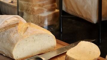 A loaf of bread on a wooden cutting board with a knife, a jar of flour, and a wooden bowl.