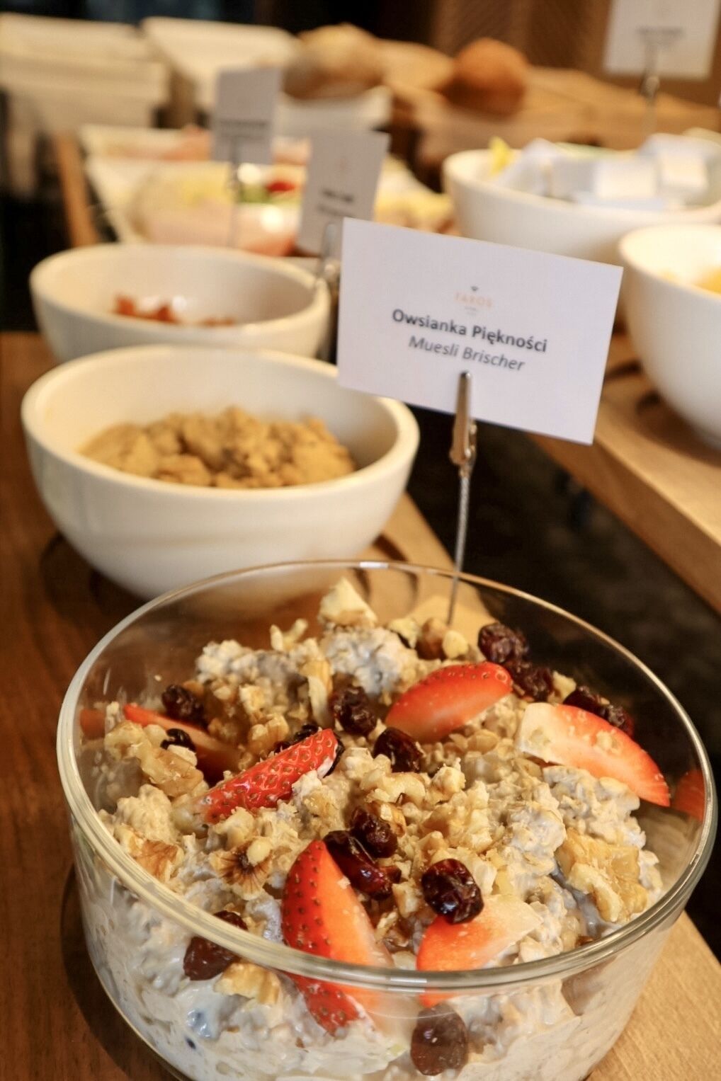A bowl of oatmeal with strawberries and raisins, labeled "Owsiana Pięknosi Muesli Brischer."