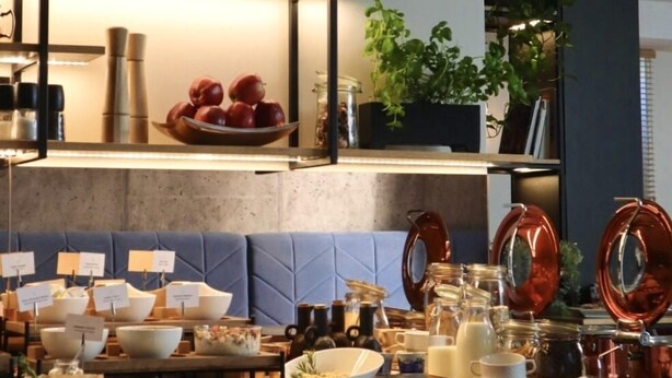A modern kitchen with a central island, shelves with plants, and a variety of kitchenware. - Hotel Faros Gdańsk Airport (Gdansk)