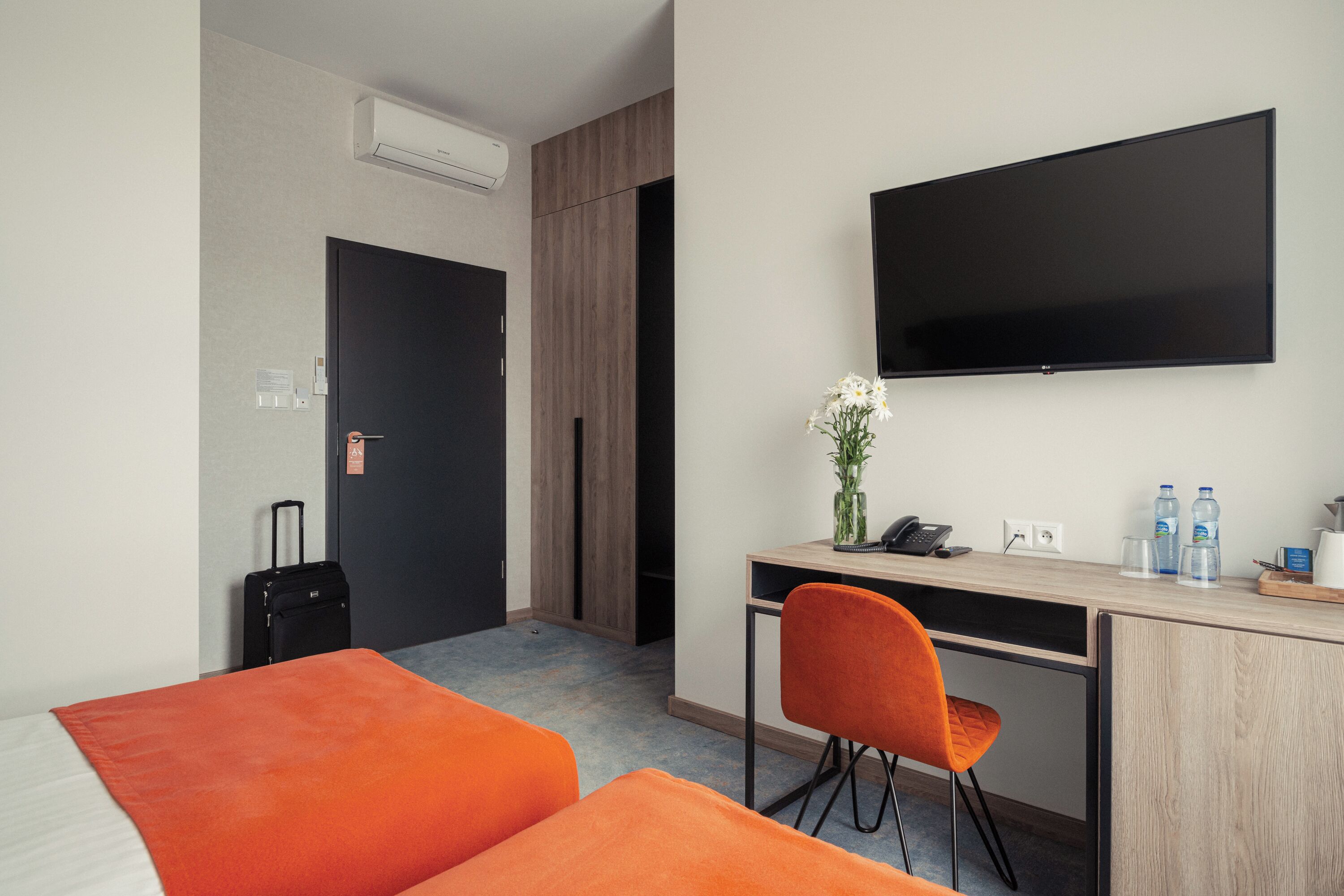 A hotel room with a bed, a desk with a chair, a television, a suitcase, and a water dispenser.