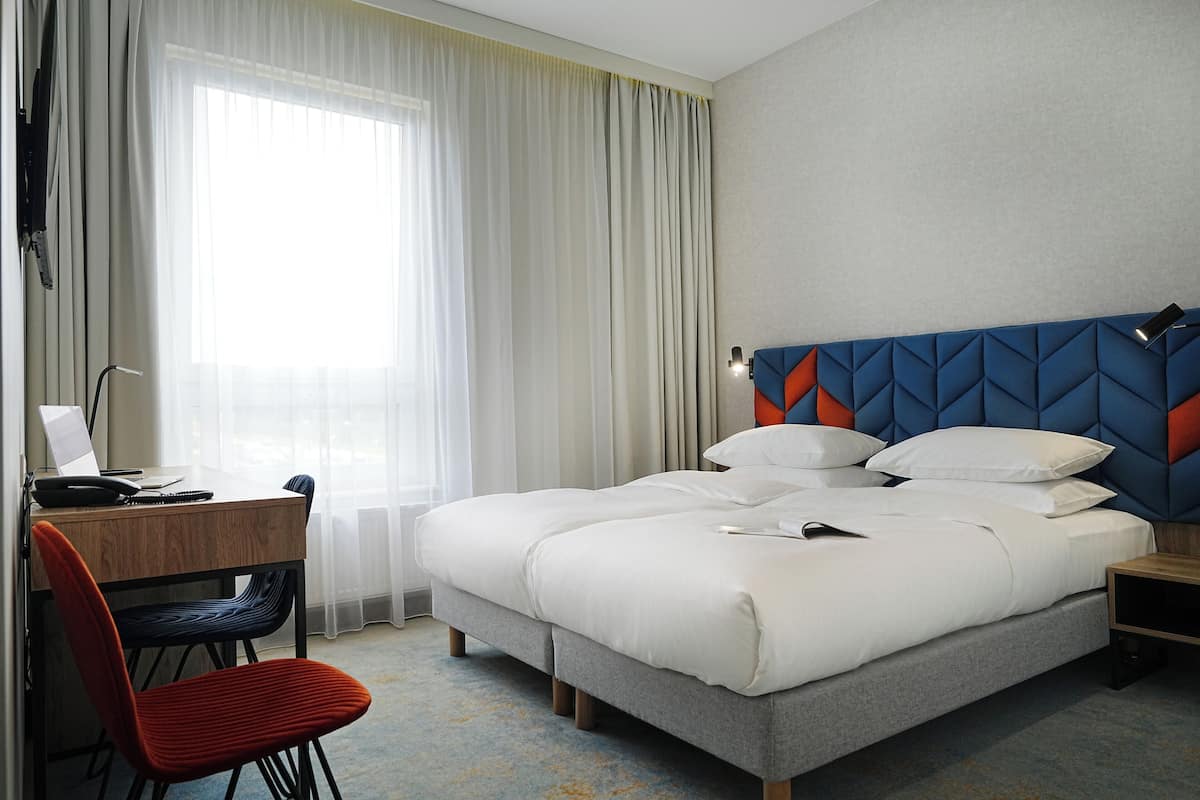 Una habitación de hotel con cama, escritorio, silla y ventana con cortinas.