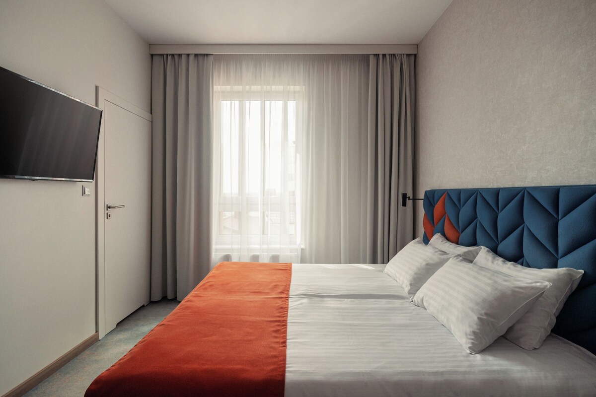 Una habitación de hotel con una cama, un televisor y una ventana con cortinas.