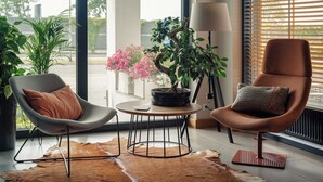 A modern living room with two chairs, a round table, a potted plant, a lamp, and a view of the outdoors. - Hotel Faros Gdańsk Airport (Gdansk)