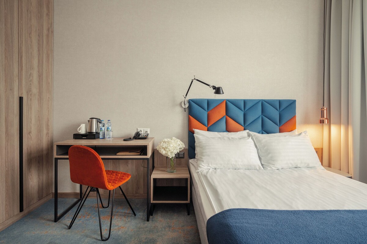 Una habitación de hotel con cama, escritorio, silla y mesita de noche con un florero.