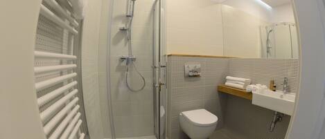 Un baño moderno con ducha de vidrio, inodoro y lavamanos con espejo.