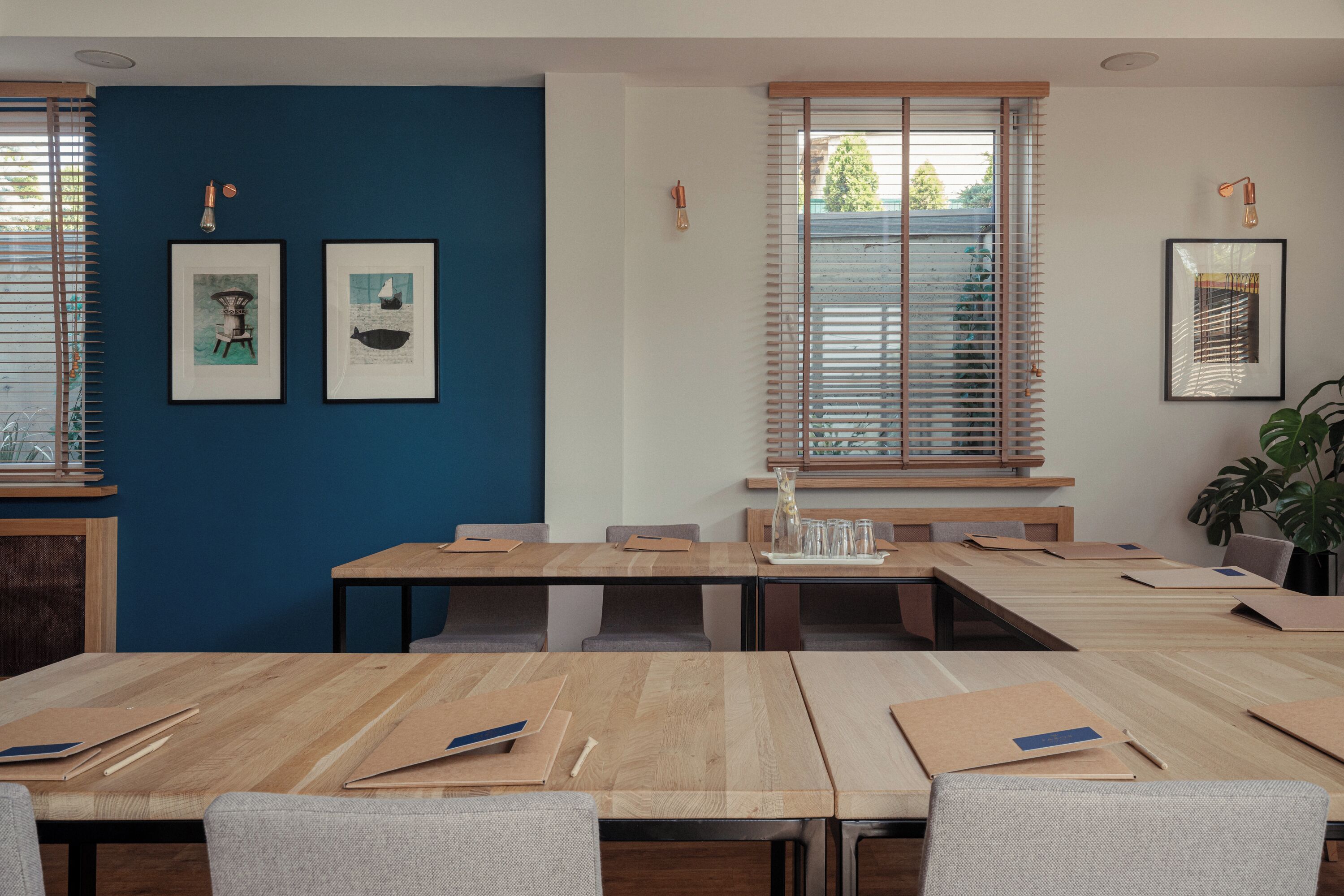 A conference room with wooden tables and chairs, framed artwork on the walls, and a window with blinds.