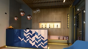 A reception area with a modern design, featuring a blue and white chevron-patterned reception desk, a wooden wall, and a wine display. - Hotel Faros Gdańsk Airport (Gdansk)