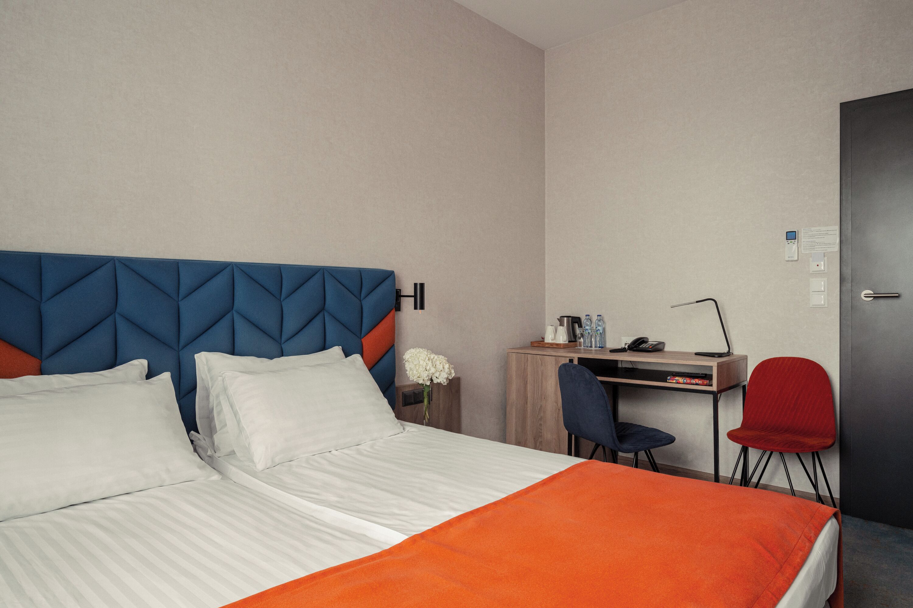 A hotel room with a bed, a desk, a chair, and a door.