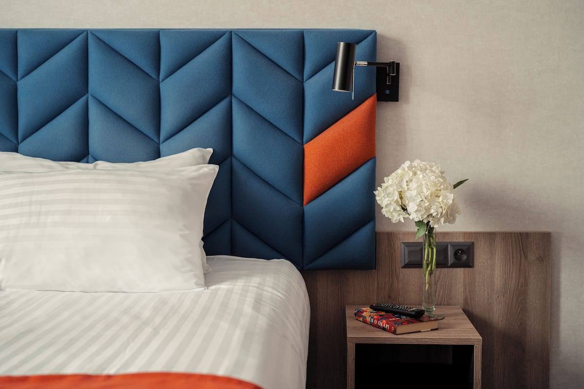 Habitación de hotel con una cama, una mesita de noche, un jarrón con flores blancas y un control remoto.