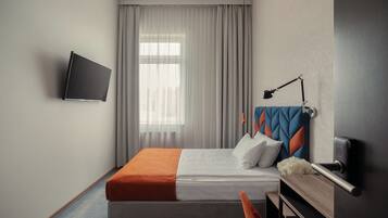 Una habitación de hotel moderna con una cama, un escritorio, una silla, un televisor montado en la pared y una ventana con cortinas.