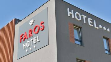 A hotel named FAROS HOTEL with a modern facade, large windows, and a prominent sign.