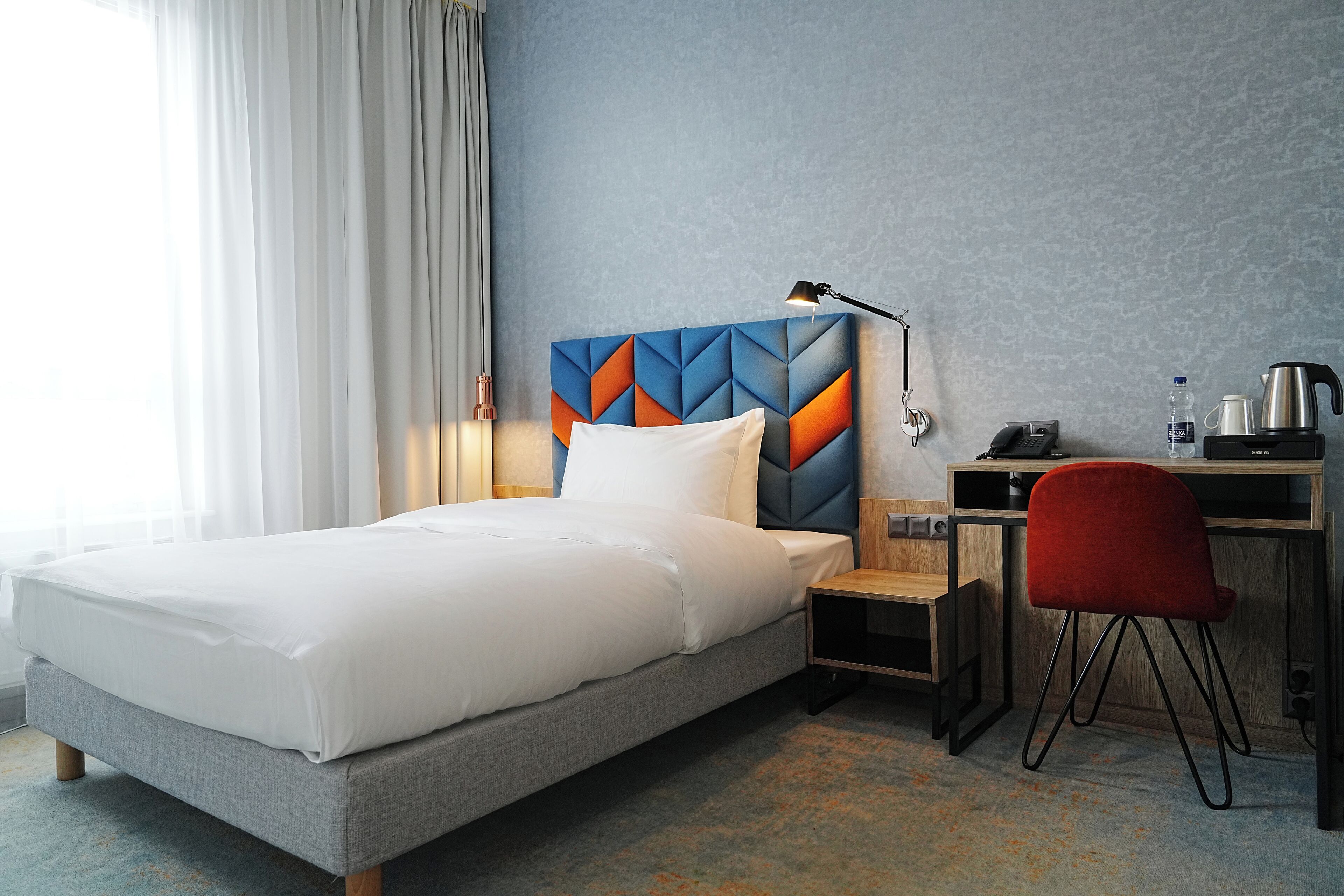 A hotel room with a bed, a desk, a chair, a lamp, and a coffee maker.