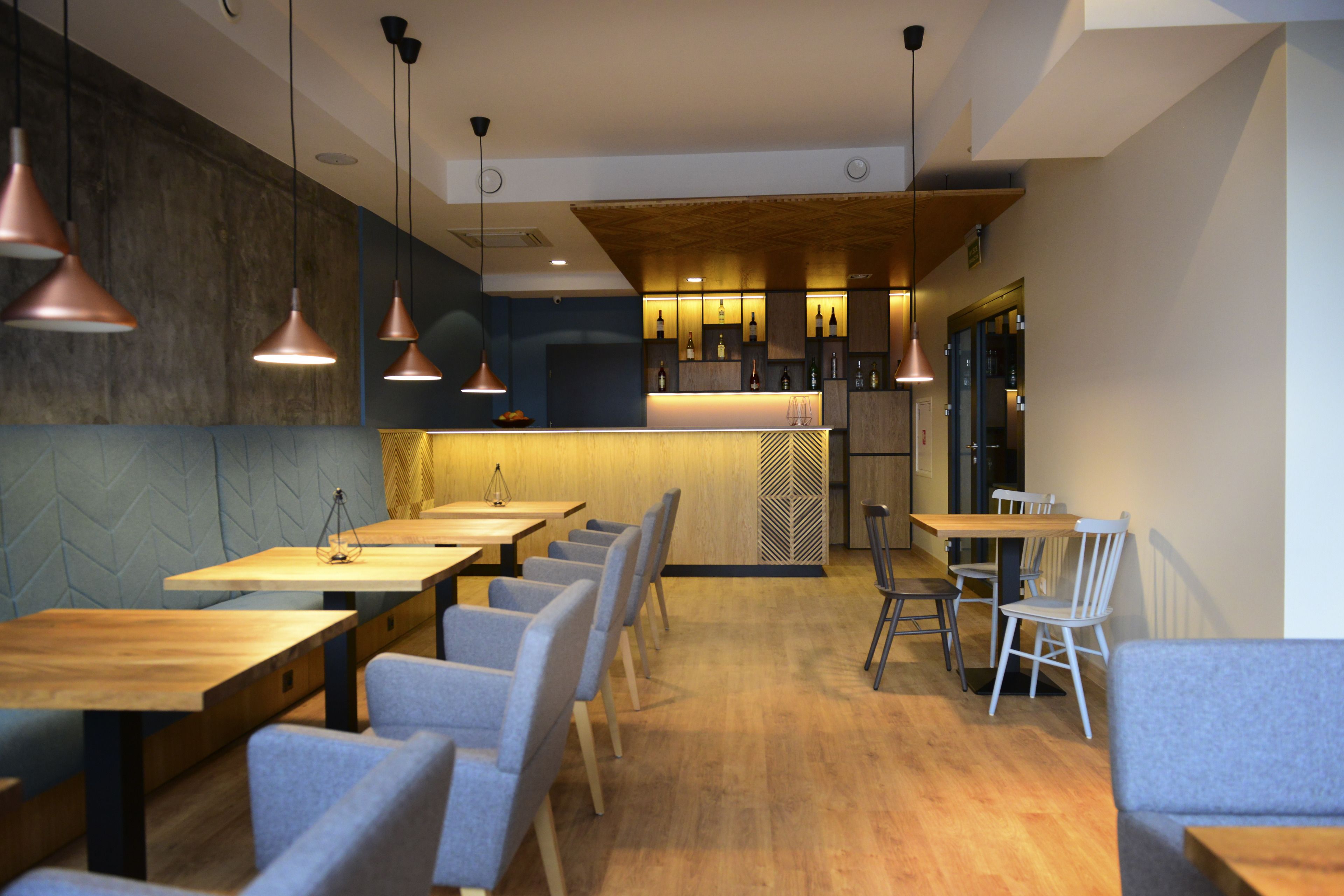 Un restaurant moderne avec des tables et des chaises en bois, un éclairage suspendu et un bar situé au fond de la salle.