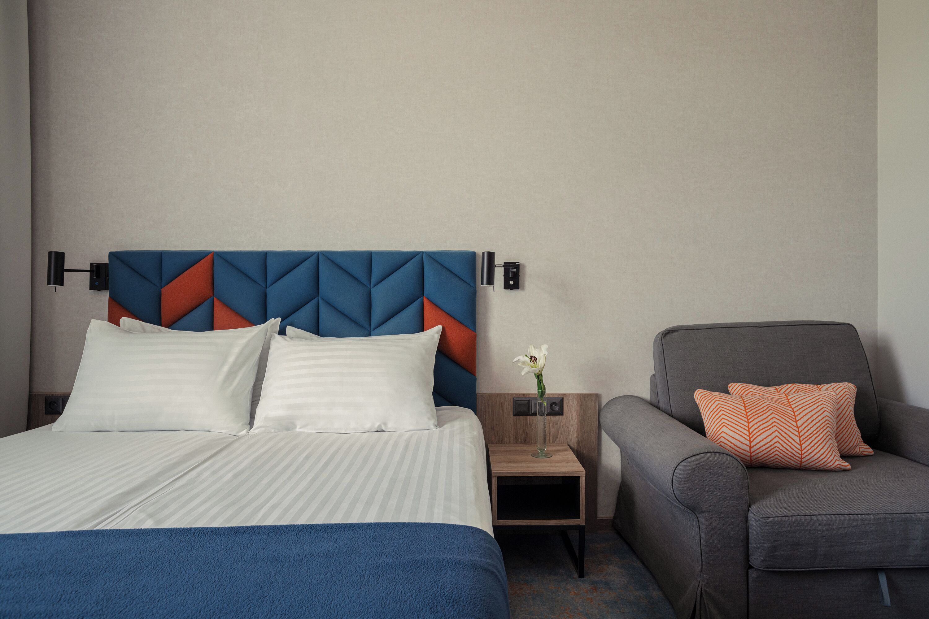 A hotel room with a bed, a nightstand, a chair, and a decorative vase.
