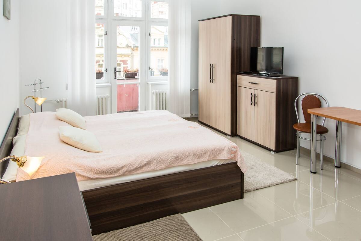 A hotel room with a bed, a desk, a chair, a wardrobe, and a television.