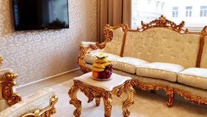 A luxurious room with a large flat-screen TV mounted on the wall, an ornate gold-framed sofa, and a small table with fruit.