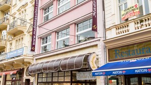 A multi-story building with a prominent pink facade, a sign for 'Madonna Apartments', and a 'Bella Sita' store with a glass facade.