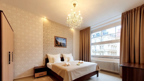 A modern bedroom with a large bed, a chandelier, a view of buildings through the window, and a radiator.