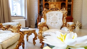 A luxurious room with ornate golden furniture, a white floral armchair, and a white flower arrangement.
