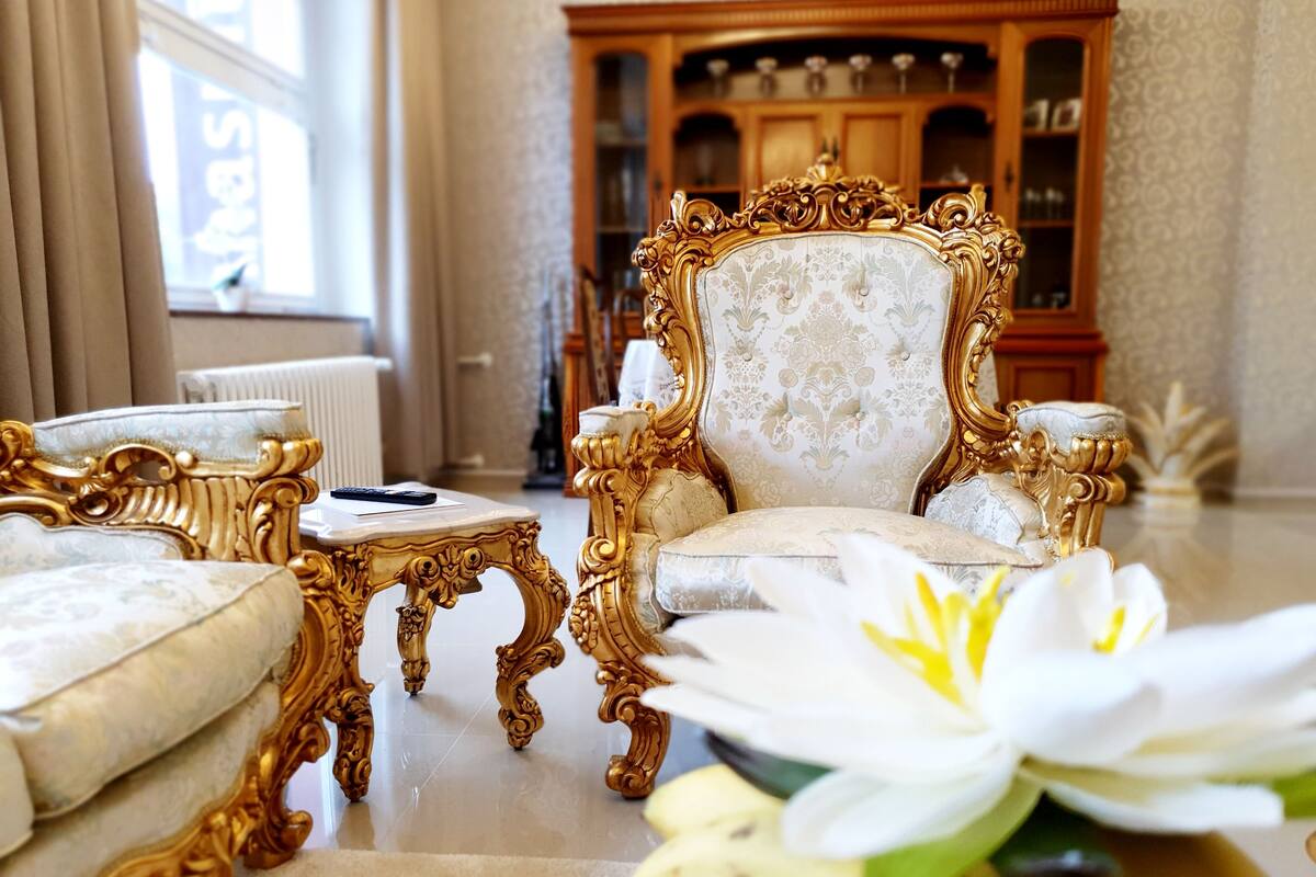 A luxurious room with ornate golden furniture, a white floral armchair, and a white flower arrangement.