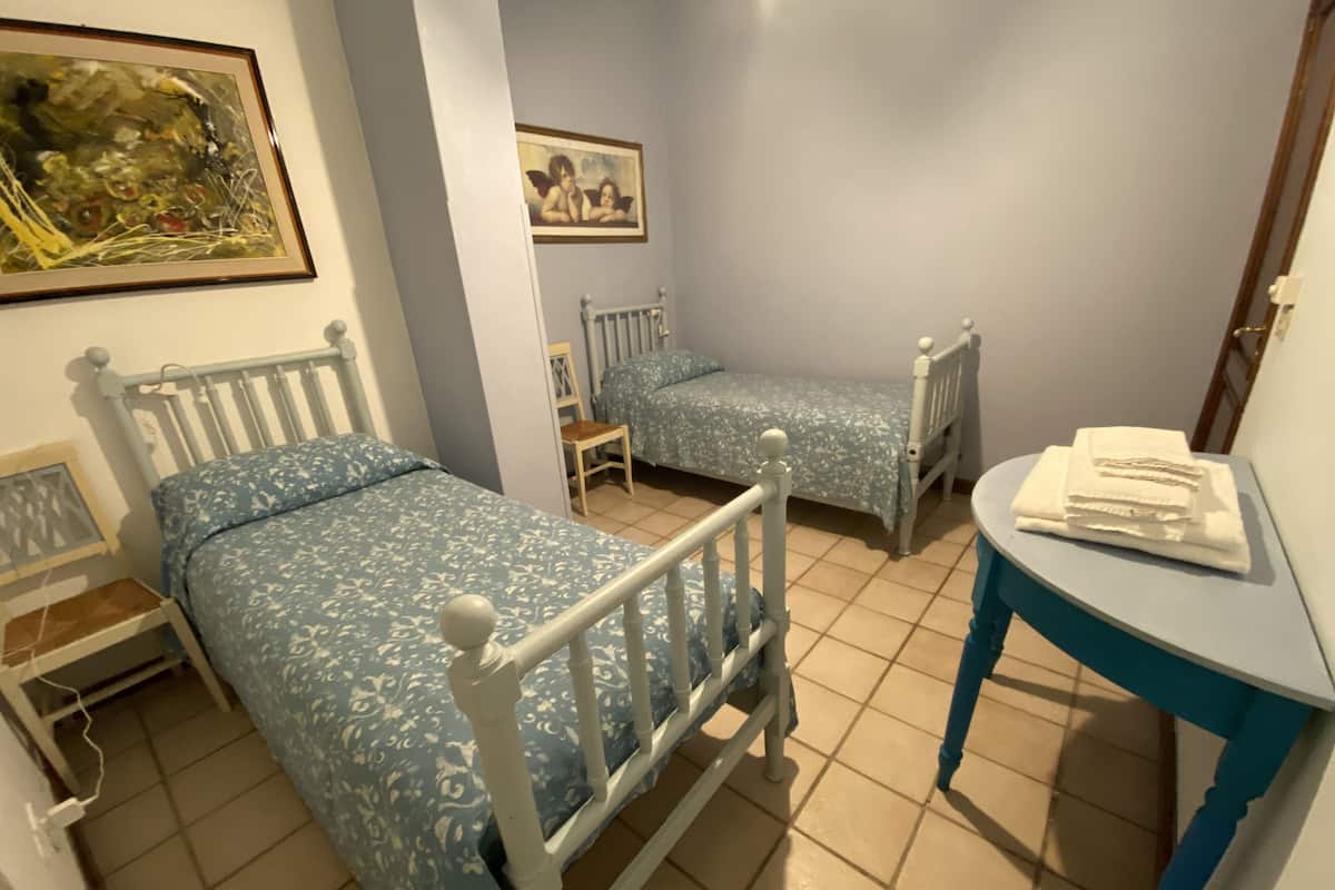 Een slaapkamer met twee eenpersoonsbedden, een tafeltje en een stoel.