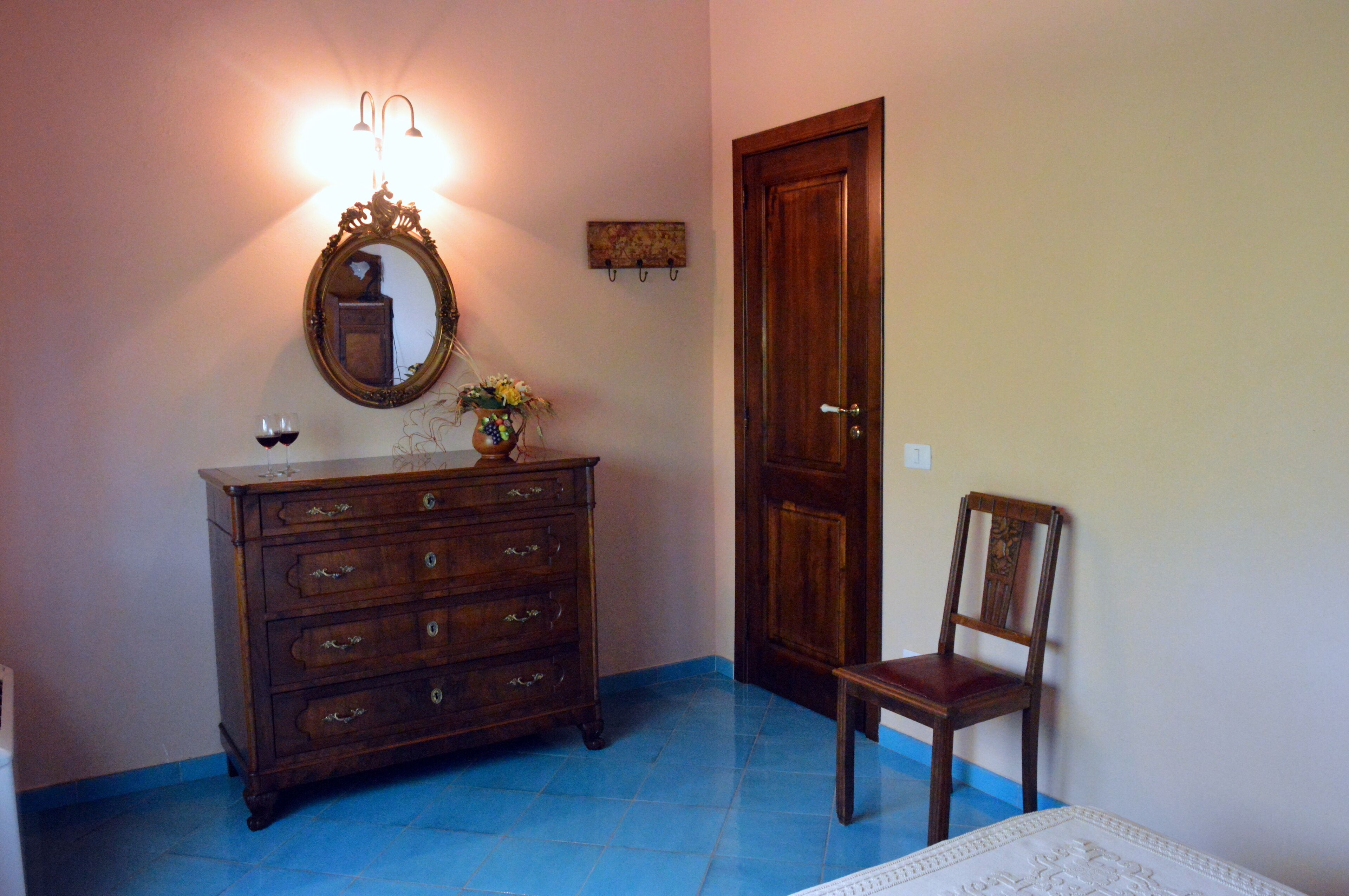 A room with a wooden dresser, a chair, a mirror, and a door.