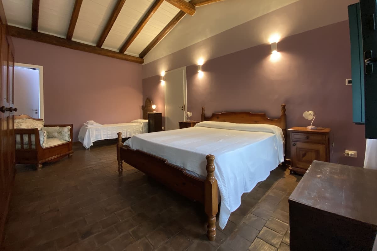 Een slaapkamer met een groot bed, twee nachtkastjes, een houten garderobe en een bankje.