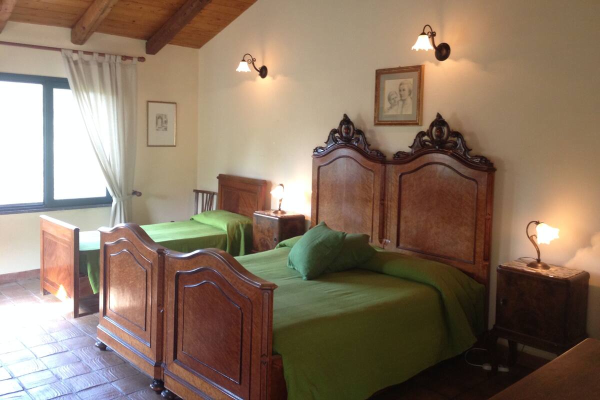Een slaapkamer met een houten bed, twee nachtkastjes, een groene spreidek en een raam met gordijnen.
